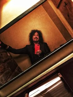 a man with long hair taking a selfie in front of a mirror holding a cell phone