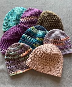 six crocheted hats laying on top of a bed next to eachother