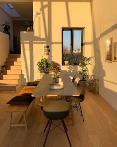 a dining room table with chairs and potted plants on top of it in front of a staircase