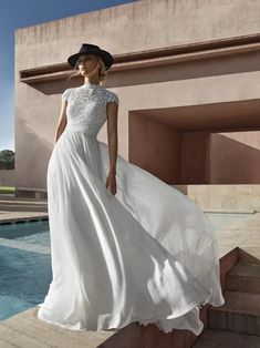 a woman in a white dress and black hat standing on steps next to a pool