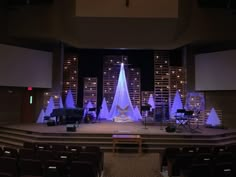 an empty church stage decorated for christmas with white trees and blue lights on the sides