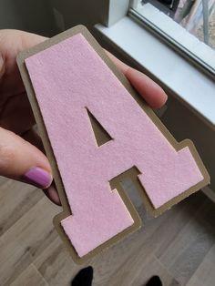 a person holding up a pink letter cut out of cardboard with the letter a on it