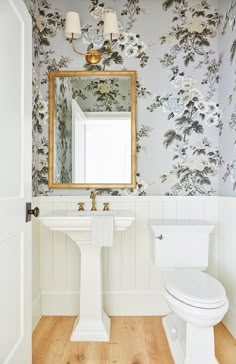 a white toilet sitting under a bathroom mirror next to a sink and a wooden floor