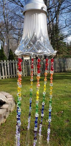 a glass wind chime hanging from a light fixture in the grass near a fence