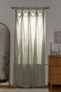 a bedroom with a mirror, dresser and window curtain in the corner that is open