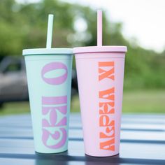 two colorful cups with straws sitting on top of a metal table in front of trees