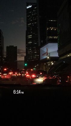 cars are driving down the street at night in front of tall buildings and skyscrapers