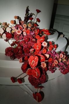 a vase filled with lots of red and pink flowers on top of a white table