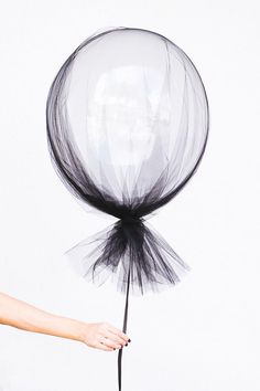 a hand holding a black and white balloon with tulle on it's tail