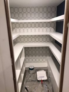 an empty closet with white shelves and wallpaper in the background, being remodeled by painters