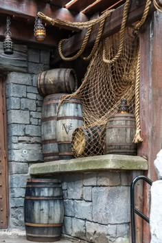 several wooden barrels are stacked on top of a stone wall with rope hanging from it