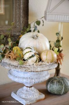 an arrangement of pumpkins and gourds in a white bowl on a table