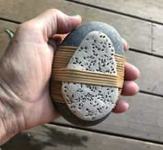 a hand holding a rock with an intricate design on it's side and a wooden band around the edge