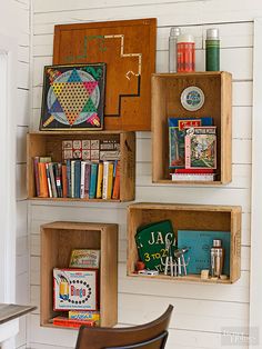 three wooden boxes filled with books on top of a white wall next to a chair