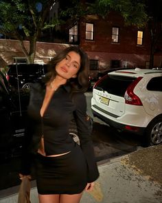 a woman is walking down the street in a short black dress and heels with her hand on her hip