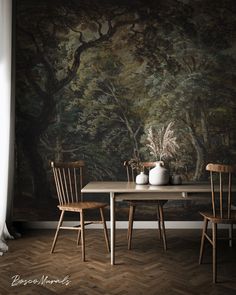 two wooden chairs sitting at a table in front of a wall with a painting on it