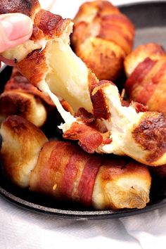 bacon wrapped hot dogs in a pan being dipped with cheese