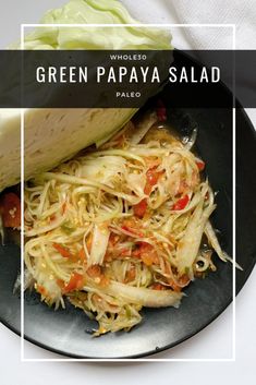 green papaya salad on a black plate with a wedge of pita bread in the background