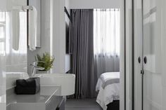 there is a bathroom with white walls and grey curtains on the window sill, along with a sink