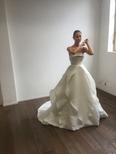 a woman in a white dress standing on a wooden floor with her arms behind her back