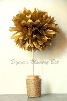 a vase filled with gold paper flowers sitting on top of a wooden table next to a white wall