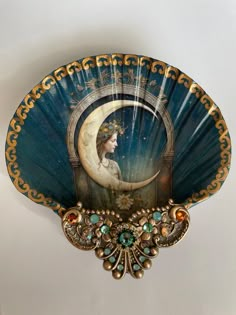 a decorative fan with an image of a woman sitting on the moon above her head