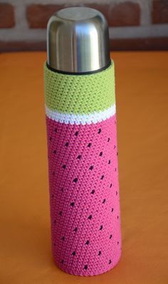 a knitted watermelon bottle cover on an orange table with a brick wall in the background