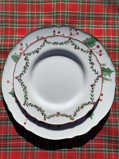 three plates with holly designs on them sitting on a plaid tablecloth covered placemat