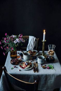 a table topped with plates and cups filled with food next to a candle on top of a table