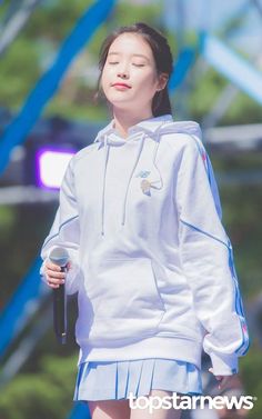 a woman in a white hoodie holding a microphone and looking up at the sky