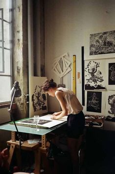 a woman sitting at a table in front of a window working on an art project