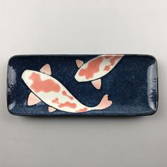 two koi fish on a blue and white plate with pink accents, against a gray background