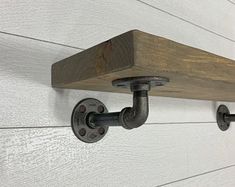 a wooden shelf mounted to the side of a wall with two pipe holders on it