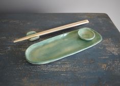 two chopsticks and a green plate on top of a wooden table with chop sticks