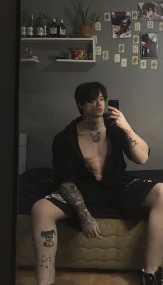 a man with tattoos sitting on a couch taking a selfie