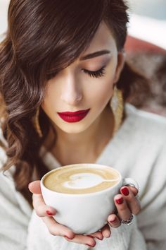 a woman holding a cup of coffee with her eyes closed and red lipstick on it