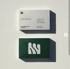 two business cards sitting side by side on top of a white surface with green lettering