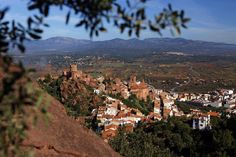 a town nestled on top of a hill surrounded by trees and mountains in the distance