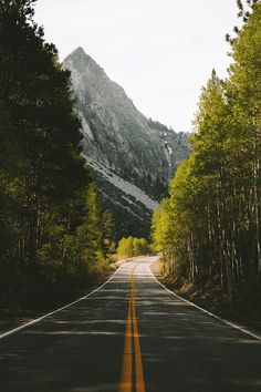 an empty road in the mountains with trees on both sides and a mountain behind it