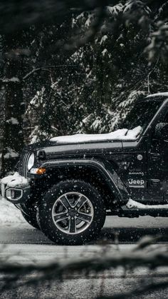 a black jeep parked on the side of a road covered in snow next to trees