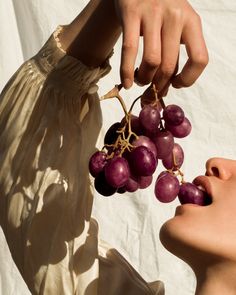 a woman holding grapes up to her face