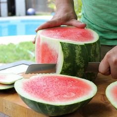 a person cutting up a watermelon on top of a wooden table next to a pool