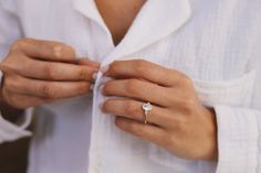 a woman wearing a white shirt is tying her wedding band with a diamond ring on her left hand