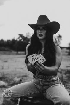 a woman sitting on top of a barrel with cards in her hand and wearing a cowboy hat