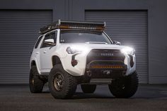 a white toyota truck parked in front of a garage door with lights on it's roof