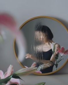 a woman standing in front of a mirror with flowers on the table next to it