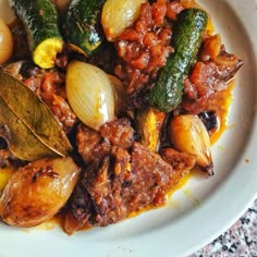 a white plate topped with meat and veggies covered in sauce on top of a table