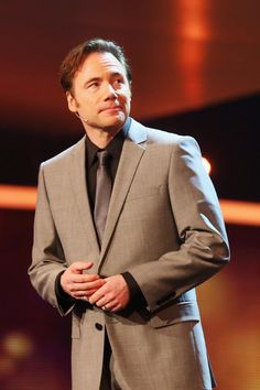 a man in a suit and tie standing on stage with his hands clasped to his chest