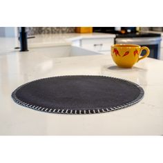 a yellow cup sitting on top of a white counter next to a black place mat