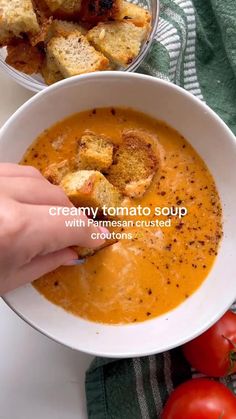 a person dipping some bread into a bowl of soup with tomatoes and croutons